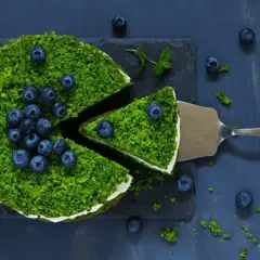 Zielony, puszysty **ciasto leśny mech na dużą blachę z serkiem mascarpone**, ozdobione borówkami. Kawałek jest już na łopatce.