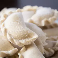 Zbliżenie na surowe, mrożone pierogi posypane mąką.