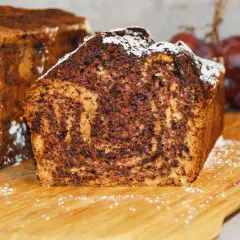Proste ciasto bananowe z olejem i kakao, z wierzchu posypane cukrem pudrem. Obok winogrona.
