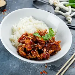 Pyszny kurczak bac bo w sosie z sezamem, podany z ryżem. Danie ozdobione kolendrą, obok pałeczki i papryczki chili.