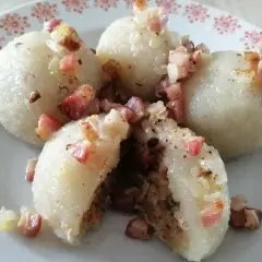 Pyszne, prawdziwe pyzy z mięsem, okraszone skwarkami i cebulką, na talerzu z czerwonym wzorem.