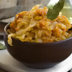 Pyszna, domowa kapusta duszona z marchewką i liściem laurowym, podana w brązowej miseczce.
