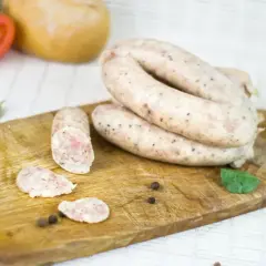 Biała kiełbasa na desce, obok pomidor, czosnek i przyprawy. Zastanawiasz się, ile czasu moczymy jelita do kiełbasy?