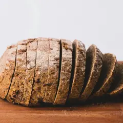 Pokrojony bochenek chleba pszennego na drewnianej desce. Zastanawiasz się, ile kalorii ma chleb pszenny?