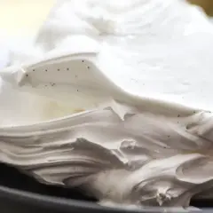 Puszysta beza szwajcarska z widocznymi ziarenkami wanilii, uformowana w eleganckie fale na ciemnym talerzu.