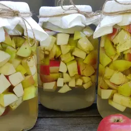 Trzy słoje z jabłkami, przygotowywane do zrobienia domowego octu jabłkowego.
