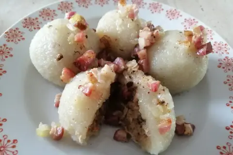 Pyszne, prawdziwe pyzy z mięsem, okraszone skwarkami i cebulką, na talerzu z czerwonym wzorem.