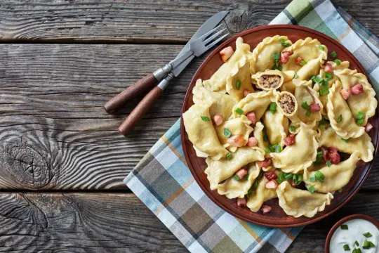 Pyszne pierogi z farszem na mięsie mielonym, posypane szczypiorkiem i skwarkami, na glinianym talerzu.