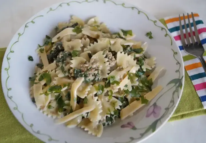 Pyszny makaron farfalle z tuńczykiem i szpinakiem, posypany świeżą natką pietruszki. Idealny na szybki obiad.