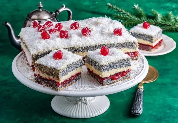 Pyszna makowa panienka z wiśniami i wiórkami kokosowymi, podana na paterze, obok srebrnego czajniczka.