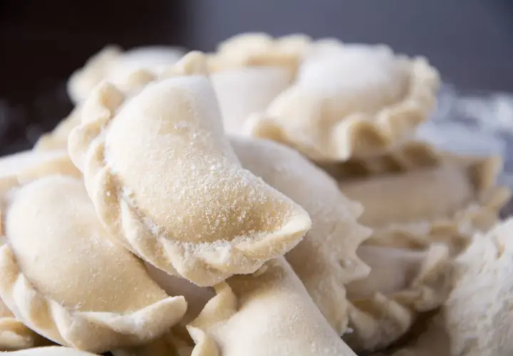 Zbliżenie na surowe, mrożone pierogi posypane mąką.