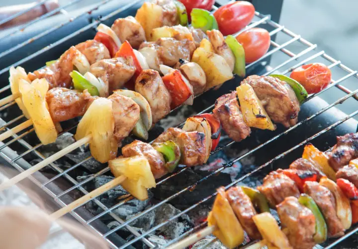 Na grillu piecze się kilka szaszłyków z kurczakiem, ananasem, papryką i pomidorkami.