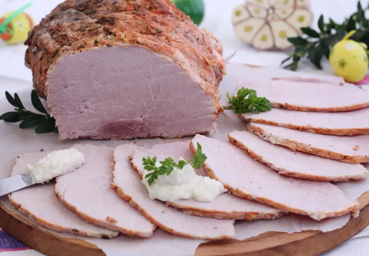 Soczysta szynka pieczona w rękawie, pokrojona w plastry, z chrzanem i natką pietruszki. Idealna na wielkanocny stół.