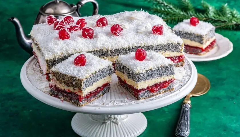 Pyszna makowa panienka z wiśniami i wiórkami kokosowymi, podana na paterze, obok srebrnego czajniczka.
