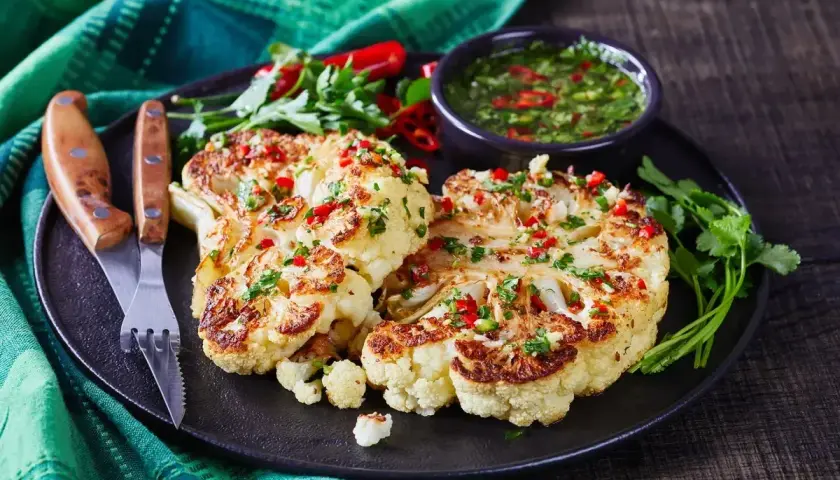 Szybkie danie z kalafiora: pieczone steki z kalafiora z sosem chimichurri, posypane chili i pietruszką.