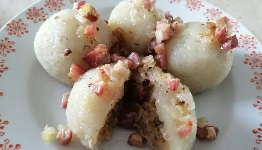 Pyszne, prawdziwe pyzy z mięsem, okraszone skwarkami i cebulką, na talerzu z czerwonym wzorem.