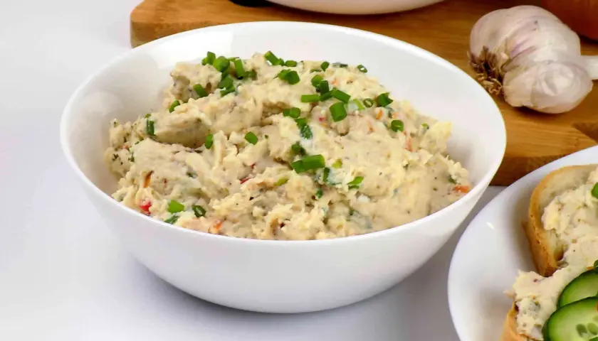 Pyszna pasta z kurczaka, posypana szczypiorkiem, gotowa do podania na świeżym pieczywie. Obok czosnek i cebula.
