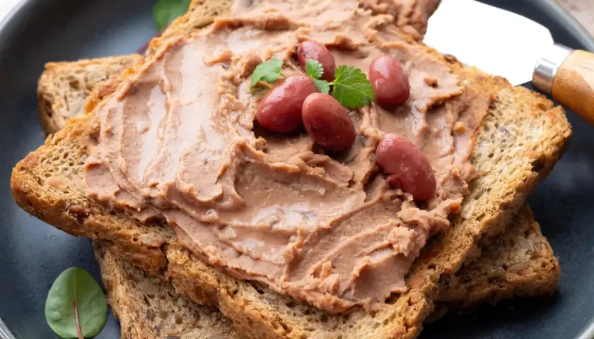 Pyszna pasta z czerwonej fasoli na chrupiących grzankach, ozdobiona fasolkami i listkami ziół. Idealna na szybką przekąskę.