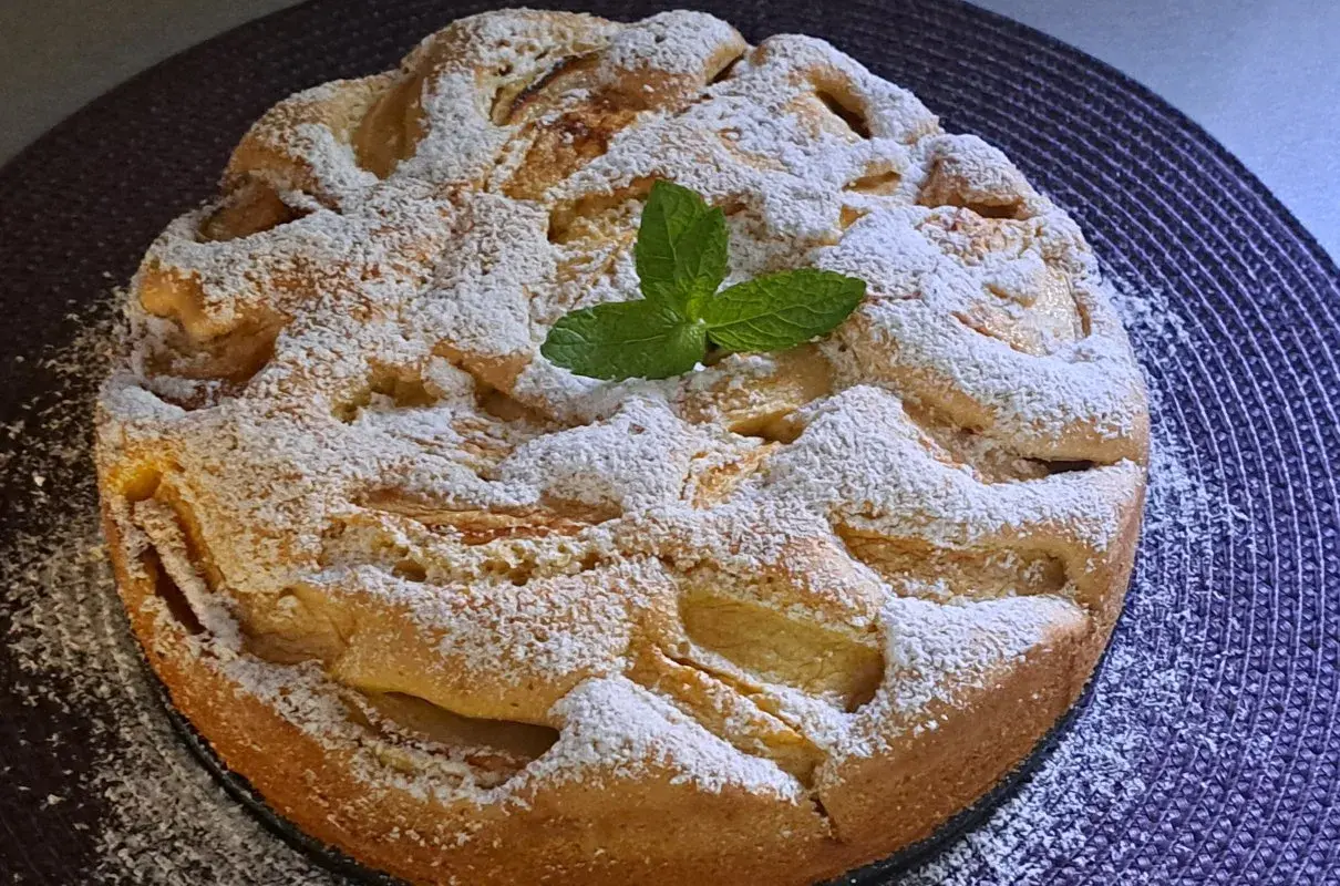 Wilgotne ciasto z jabłkami na oleju, posypane cukrem pudrem i ozdobione listkiem mięty. Idealne na deser.