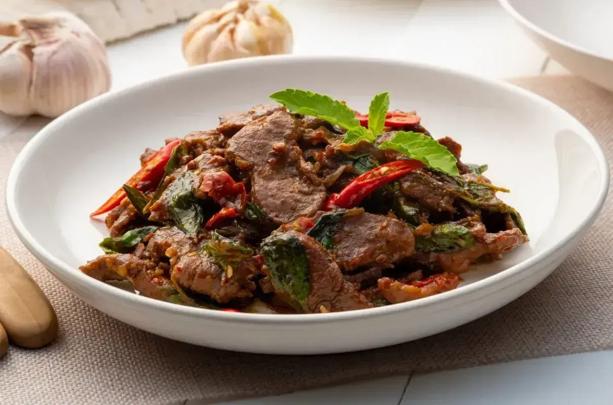 Aksamitne kawałki wołowiny z bazylią i papryczką chili, aromatyczne wołowina po tajsku, podane w białej misce.