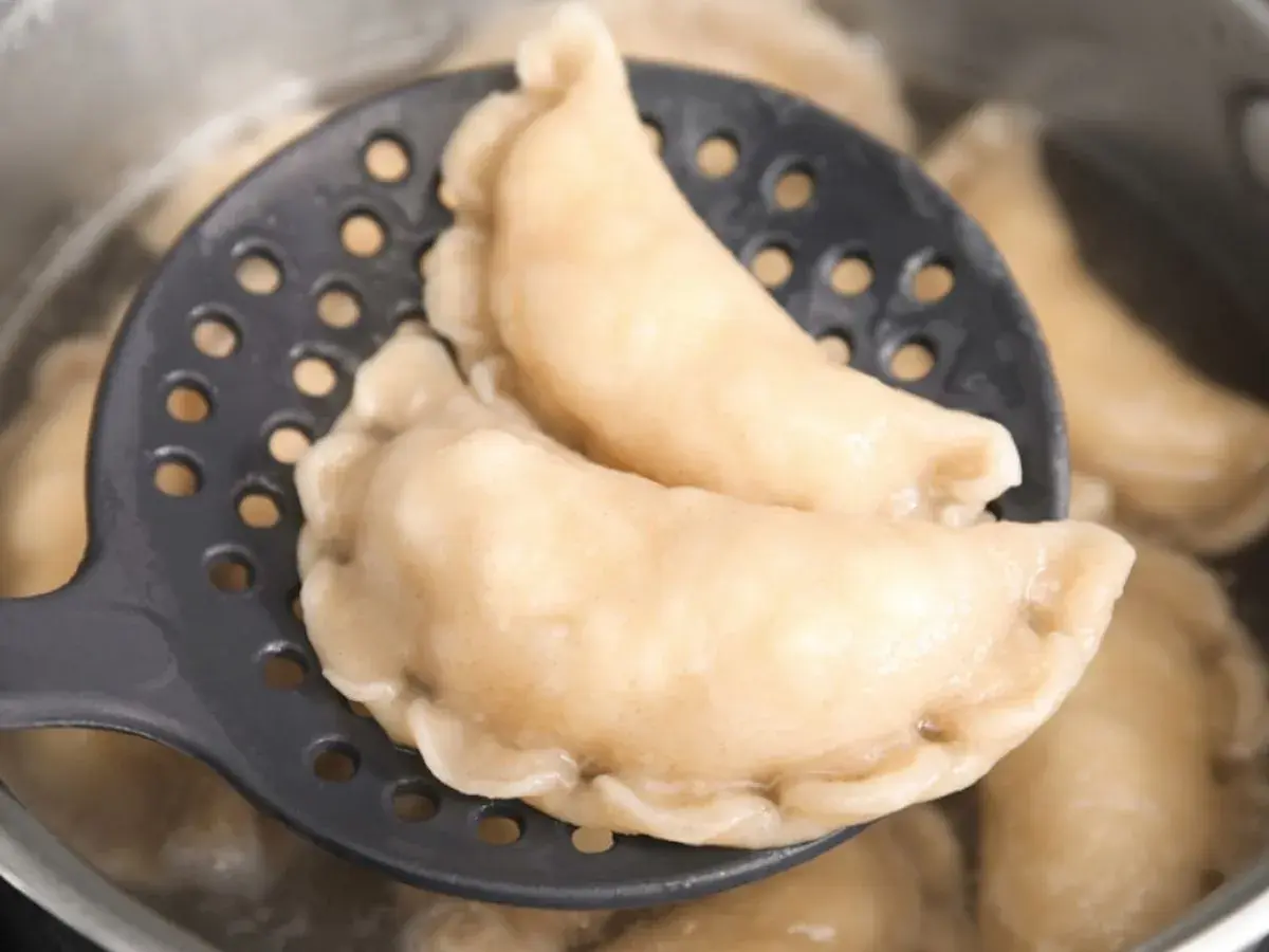 Gotowe pierogi z serem na łyżce cedzakowej, gotujące się w garnku. Idealne, by pokazać, jak zrobić pierogi z serem.