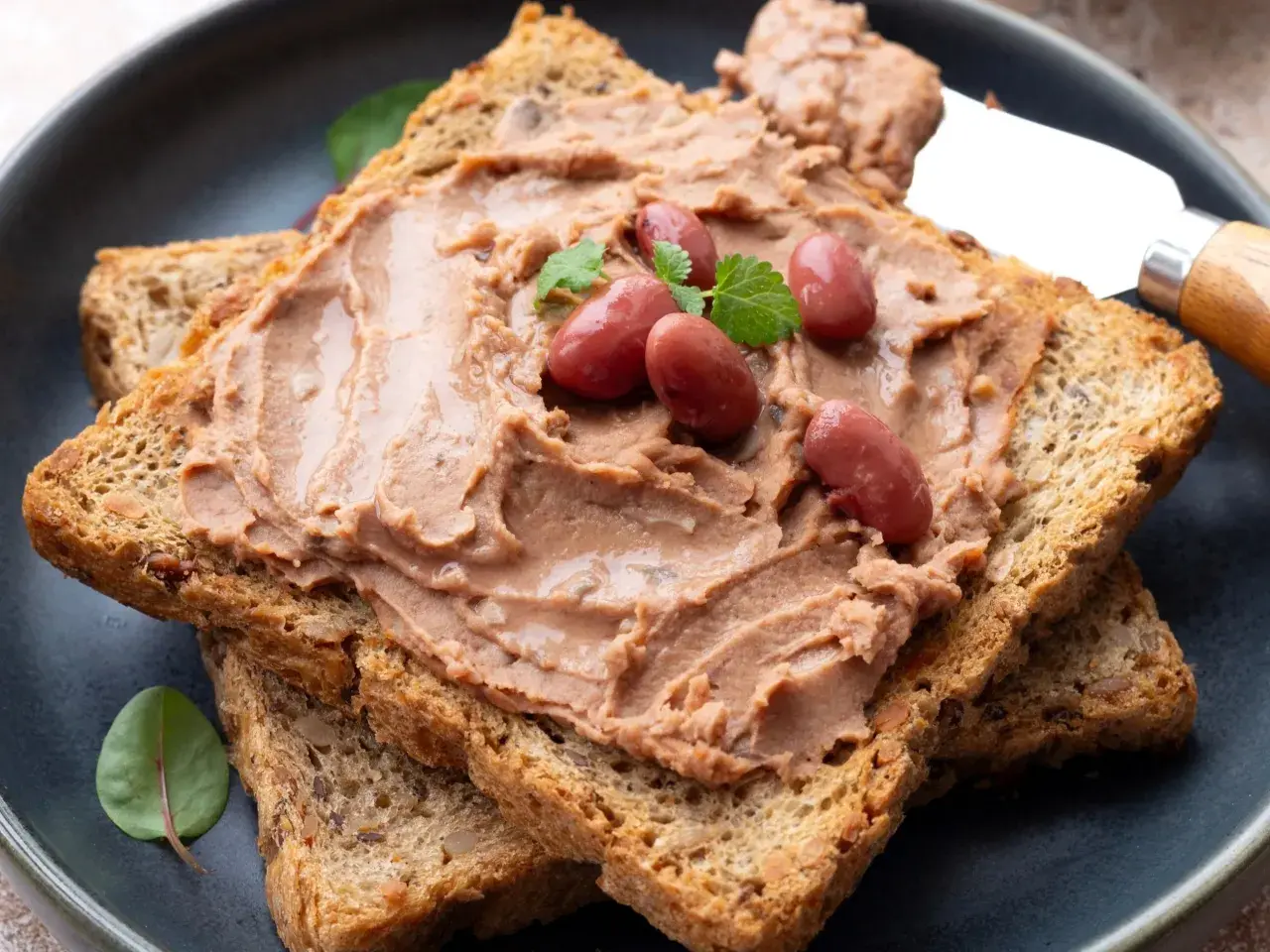 Pyszna pasta z czerwonej fasoli na chrupiących grzankach, ozdobiona fasolkami i listkami ziół. Idealna na szybką przekąskę.