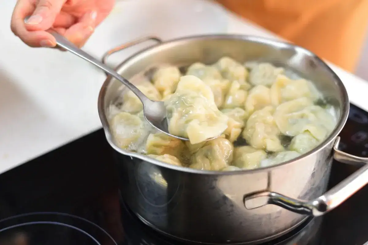 Gotujesz domowe pierogi w garnku. Łyżka wyciąga jednego, by sprawdzić, czy są gotowe do zamrożenia.
