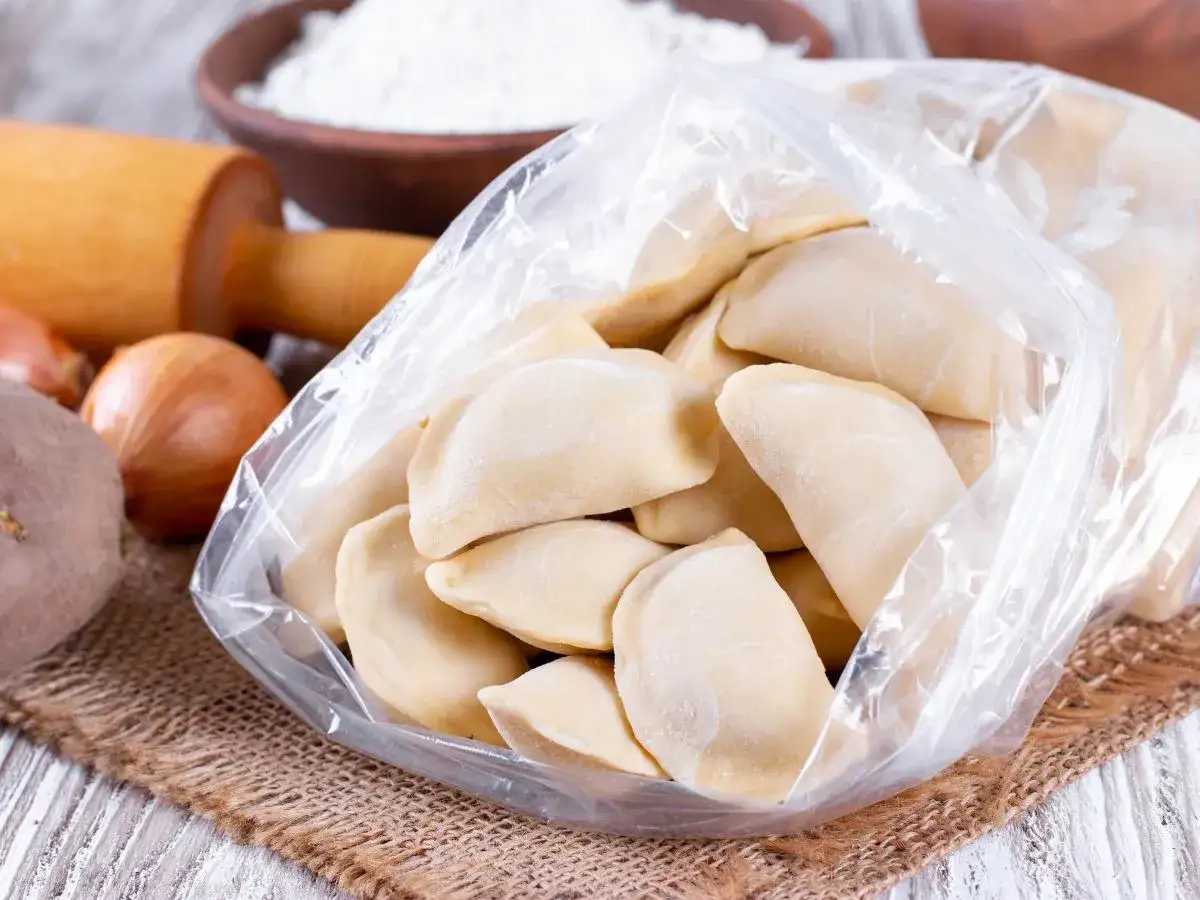 Surowe pierogi w woreczku, gotowe do zamrożenia. Obok wałek, cebula i mąka. Czy ciasto na pierogi można zamrozić? Tak!
