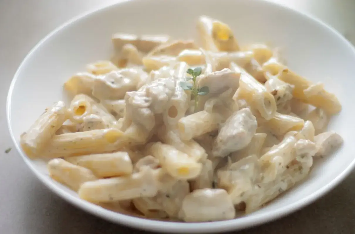 Penne z kurczakiem w kremowym sosie śmietanowo-serowym, udekorowane gałązką ziół. Pyszne danie gotowe do podania.