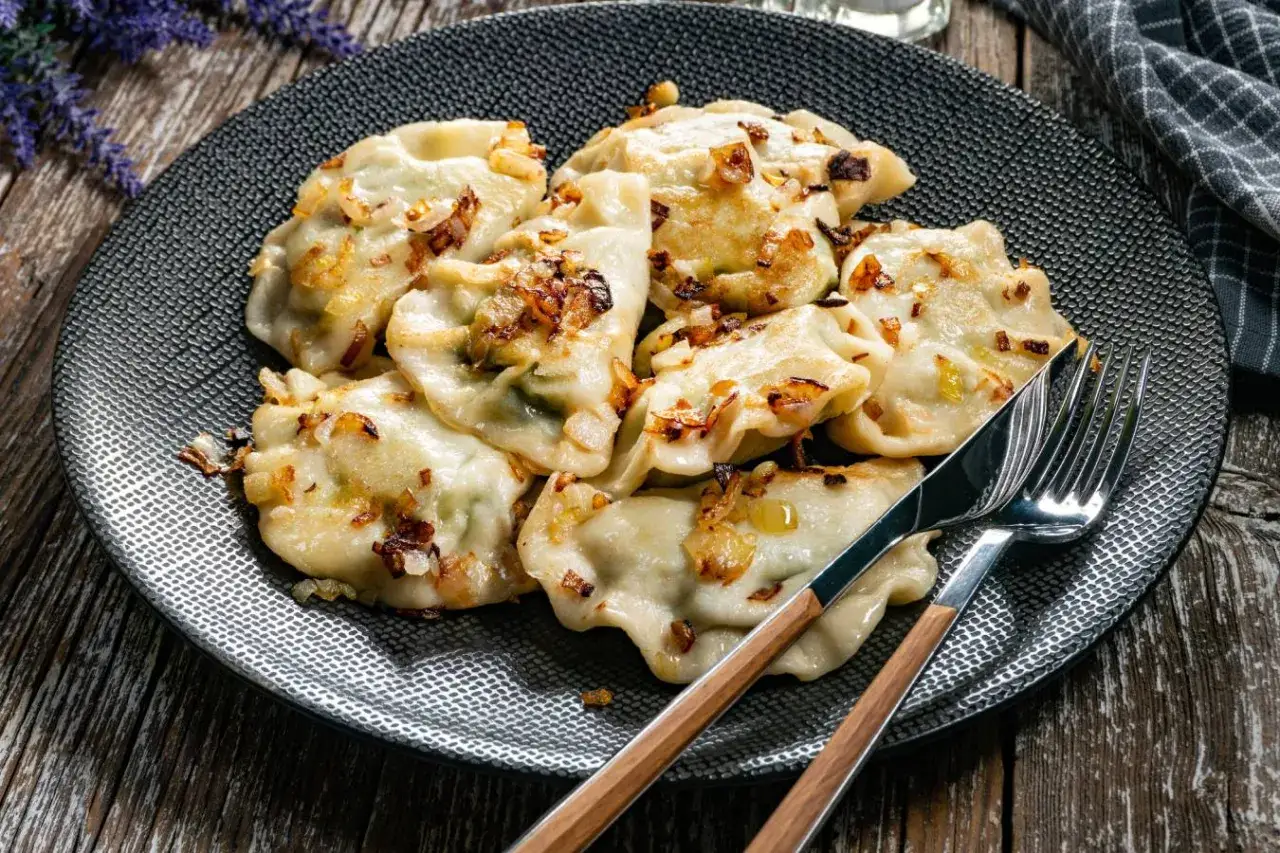 Pyszne pierogi z cebulką, idealne do gotowania w wrzącej wodzie. Na talerzu z widelcem i nożem.