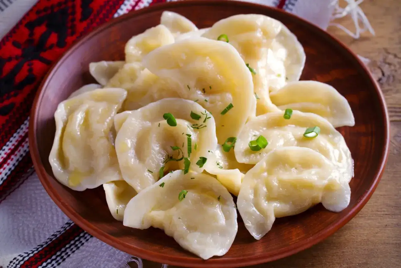 Pyszne, parujące pierogi na glinianym talerzu, posypane szczypiorkiem. Idealne, gdy wrzuca się je do gotującej wody.