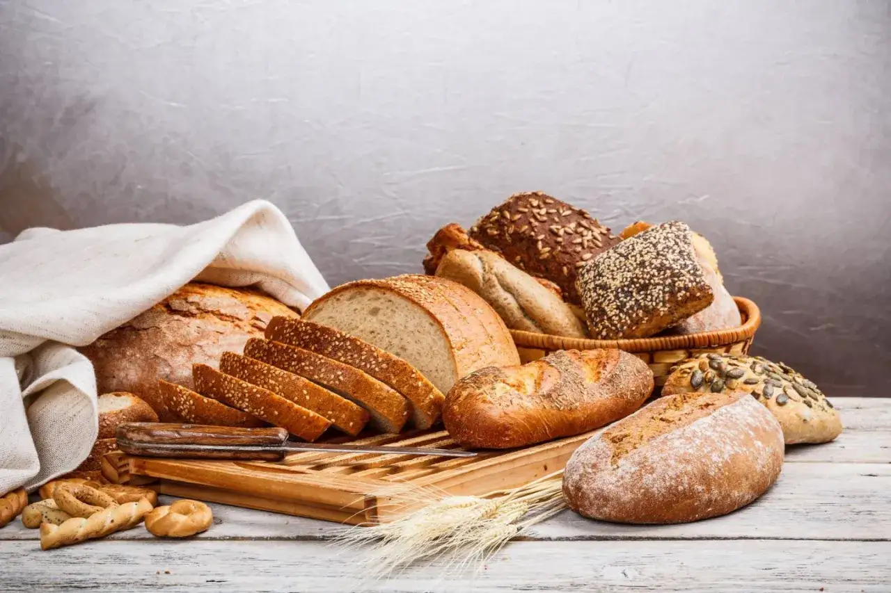 R&oacute;żnorodne pieczywo, od bochenk&oacute;w po bagietki, ułożone na desce. Idealne, by dowiedzieć się, jak podgrzać chleb w piekarniku.