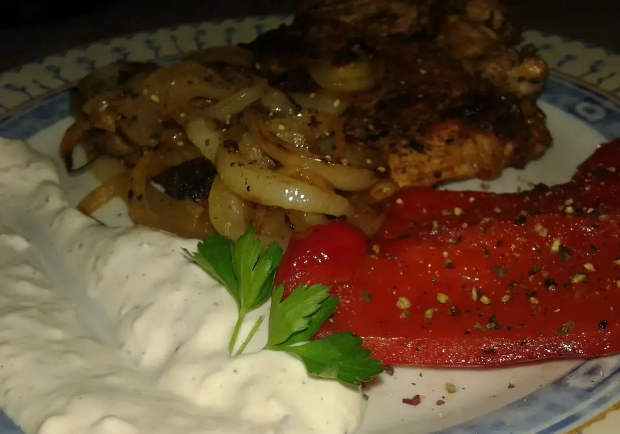 Pyszny tomahawk wieprzowy z karmelizowaną cebulką, pieczoną papryką i kremowym sosem.