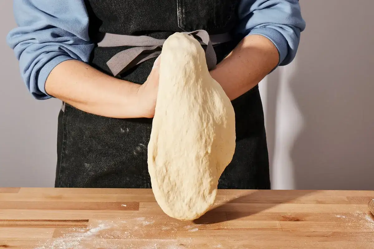 Ręce formują elastyczne ciasto na pizzę. Proste ciasto na pizzę zawsze wychodzi, gdy jest tak starannie przygotowane.