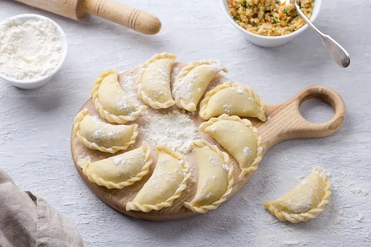 Surowe pierogi ułożone na desce. Czy ciasto na pierogi można zrobić dzień wcześniej? Tak, można je przechowywać w lodówce.