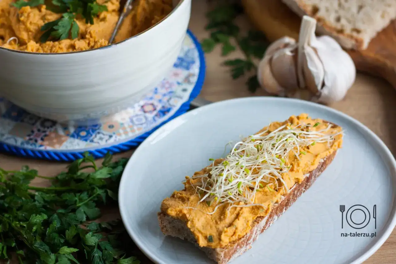 Pyszna pasta z kurczaka na kromce chleba, posypana kiełkami. Obok miska z pastą i czosnek.