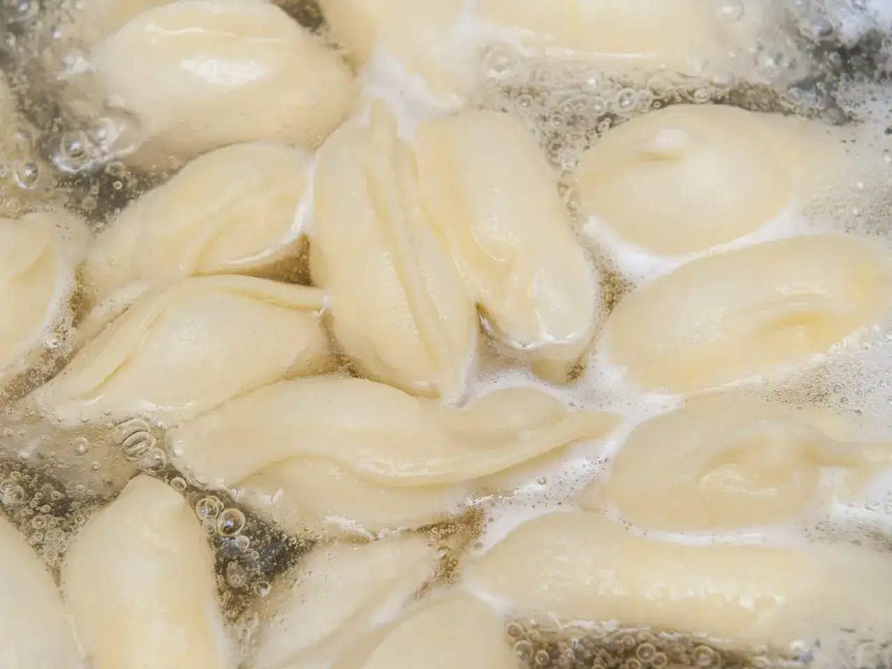 Gotowane pierogi w wodzie, aby się nie skleiły, należy mieszać. Widać bąbelki pary i pianę.