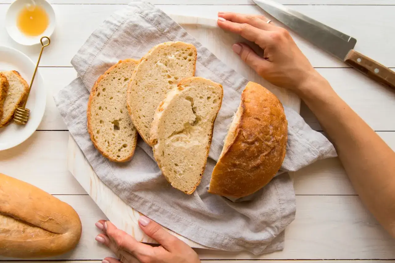 Jak podgrzać chleb w piekarniku? Pokrojony bochenek i kromki na desce, obok mi&oacute;d i n&oacute;ż.