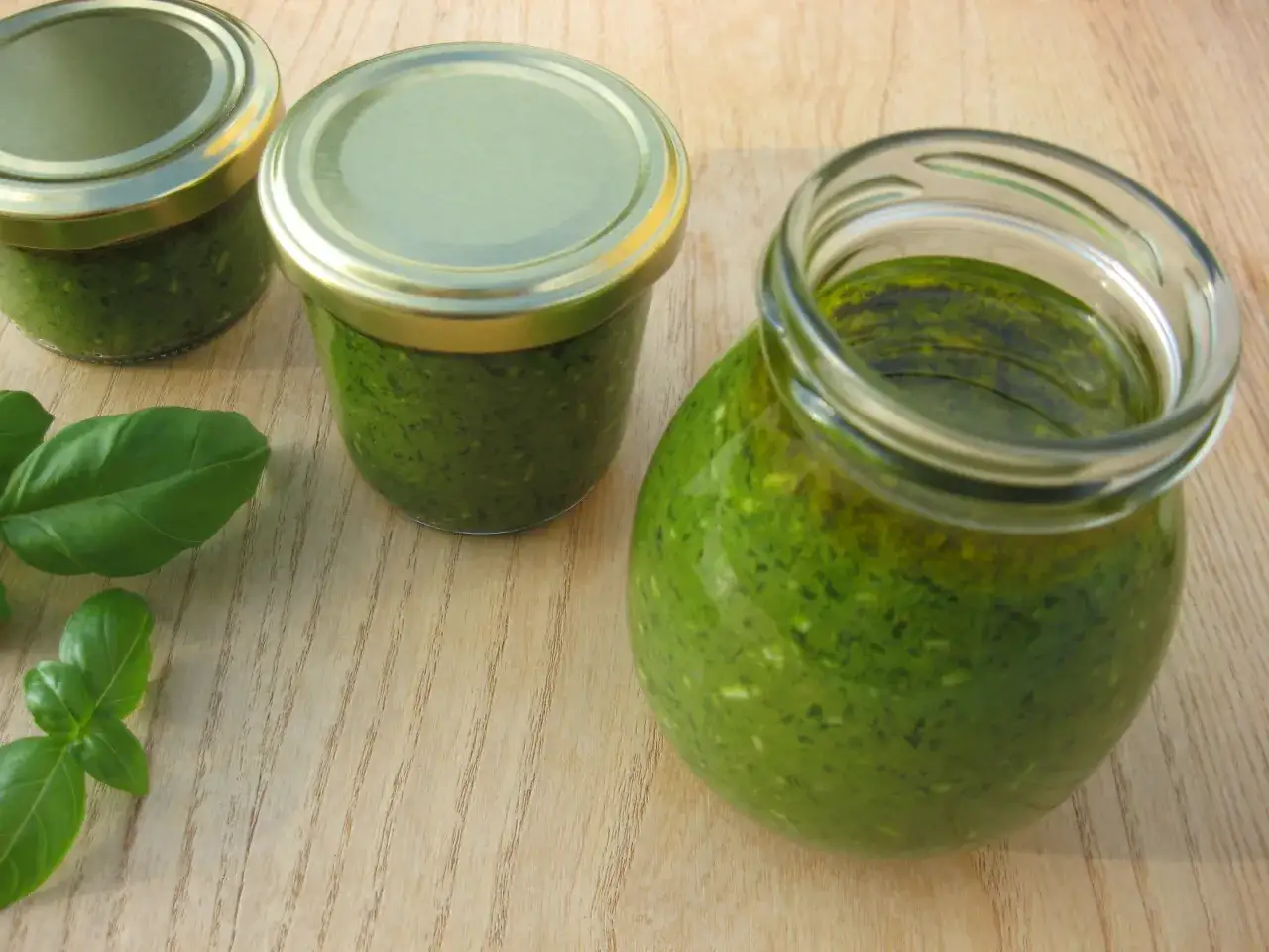 Słoiki z domowym pesto z bazylii, gotowe na zimę. Świeże liście bazylii obok.