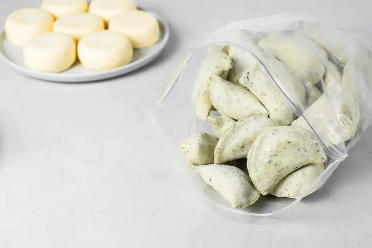 Gotowe do mrożenia domowe pierogi w woreczku, obok talerz z okrągłymi serkami. Idealne, by dowiedzieć się, jak mrozić domowe pierogi.