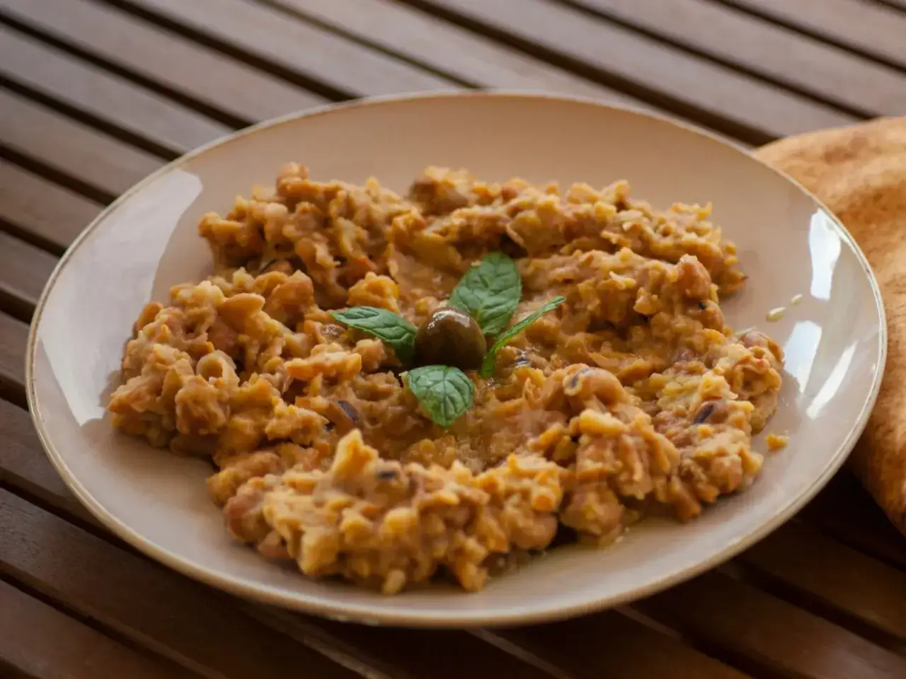 Pyszna pasta z ciecierzycy, udekorowana oliwką i miętą, podana na talerzu na drewnianym stole.