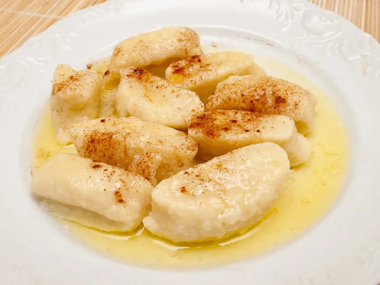 Pyszne pierogi leniwe, polane masłem i posypane cynamonem. Idealne na szybkie śniadanie lub deser, pokazujące, jak się robi pierogi leniwe.
